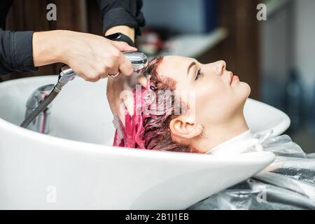 Coiffeur laver les cheveux teints roses de la femme dans l'évier, gros plan. Banque D'Images