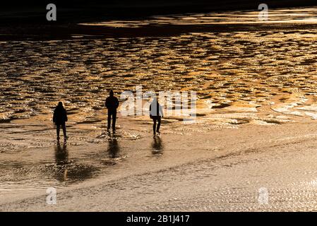 Les gens qui marchent à travers la plage de Porth à marée basse silhouetted par le soleil couchant à Newquay dans Cornwall. Banque D'Images