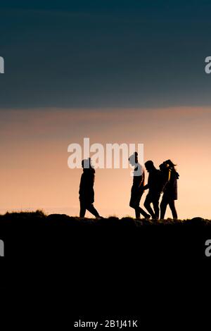 Un groupe d'amis marchant à la maison comme le soleil se couche à la fin de la journée. Banque D'Images