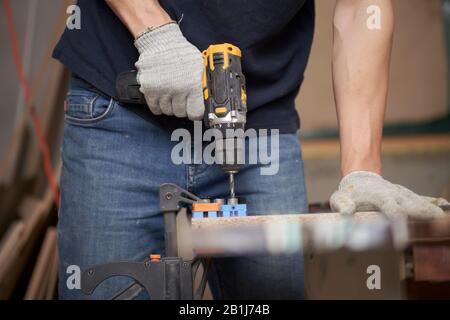 Homme charpentier avec foreuse et planche en atelier, gros plan Banque D'Images