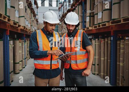 Les jeunes travailleurs se sont concentrés dans l'entrepôt pour discuter du travail sur la tablette numérique Banque D'Images