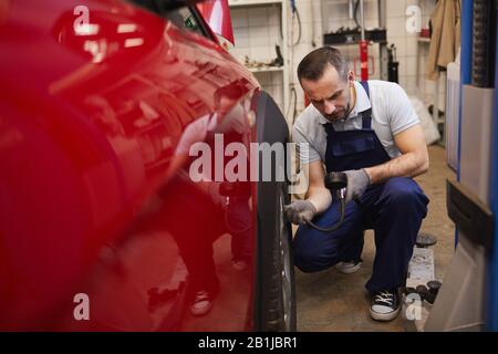 Portrait du mécanicien de voiture vérifiant la pression dans les pneus lors de l'inspection du véhicule dans un garage, espace de copie Banque D'Images