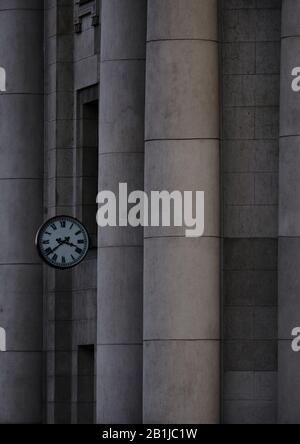 Horloge accrochée sur un bâtiment avec des colonnes en béton et une façade Banque D'Images