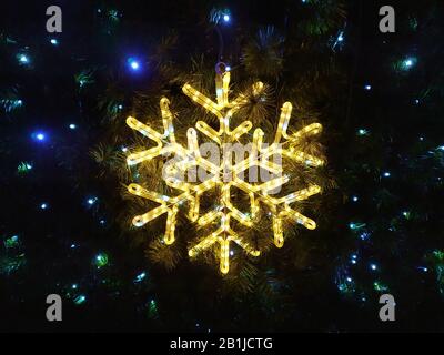 Décoration sous forme de boule de neige lumineuse jaune, qui pleurent sur un arbre de Noël sur fond d'aiguilles et de lumières bleues Banque D'Images