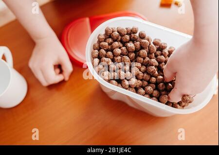 La main de l'enfant dans un pot de flocons de chocolat avec des boules de petit déjeuner. Le plaisir des enfants avec la nourriture. Banque D'Images