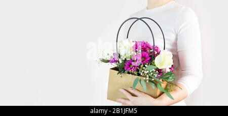 La fille tient un panier dans ses mains avec un beau bouquet de roses et de chrysanthèmes. Livraison de fleurs, bouquet d'un fleuriste, arrangement de fleurs Banque D'Images