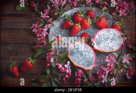 Flatlay - Contexte de l'alimentation en bois sombre vide avec du fruit du dragon, les fraises et les fleurs roses, l'espace de copie pour le texte Banque D'Images