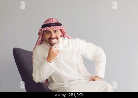 Portrait de l'homme arabe assis sur une chaise sur un fond gris Banque D'Images