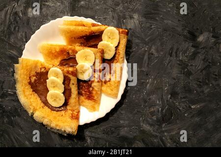 Crêpes fraîches avec pâte de chocolat et banane sur fond gris avec espace de copie. Crêpes de style russe pour la semaine Pancake. Banque D'Images