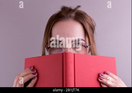 Une jeune fille dans les verres est en train de lire un livre. Femme sur un fond gris. Le concept de l'éducation et de l'information. Espace libre pour le texte Banque D'Images