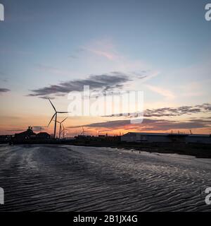 Crépuscule au port de Tilbury, Essex, Royaume-Uni. Vue sur le coucher du soleil de la marée basse de la Tamise et des éoliennes tournant en arrière-plan. Banque D'Images