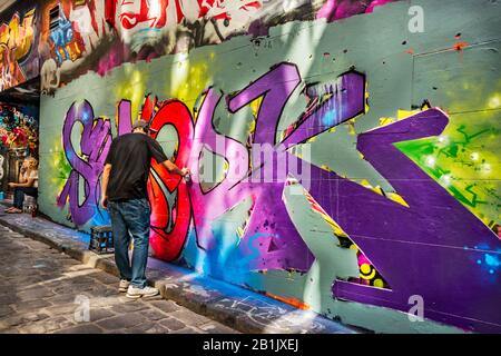 Un jeune homme vaporise de la peinture sur le mur des graffitis, Hosier Street, Melbourne Lanes, Melbourne, Victoria, Australie Banque D'Images