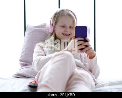 La vie moderne de la génération Z. adolescence fille en pyjama et écouteurs dans la chambre sur le lit écoute la musique d'un smartphone. Banque D'Images