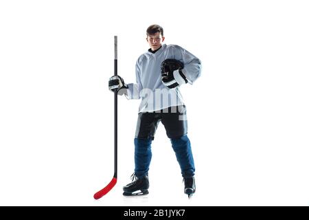 Notation. Jeune joueur de hockey masculin avec le bâton sur la cour de glace et fond blanc. Sportif portant de l'équipement et du casque pratiquant. Concept de sport, mode de vie sain, mouvement, mouvement, action. Banque D'Images