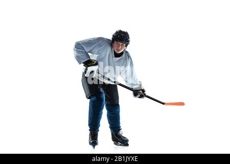 Notation. Jeune joueur de hockey masculin avec le bâton sur la cour de glace et fond blanc. Sportif portant de l'équipement et du casque pratiquant. Concept de sport, mode de vie sain, mouvement, mouvement, action. Banque D'Images