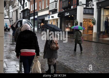 Piétons et commerçants marchant dans la pluie shopping avec des parasols le long de Guildford High Street, Guildford, Surrey, Royaume-Uni - Banque D'Images