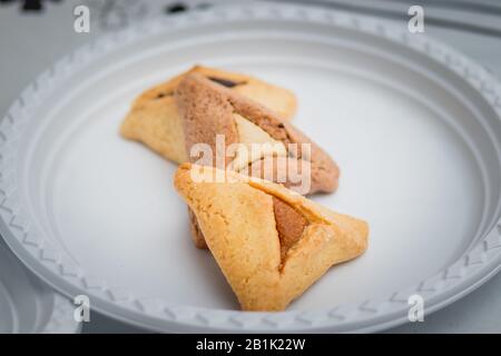 Hamantaschen. (ozen haman). La nourriture juive pour Purim. Pâte croustillante triangulaire, farcie de dattes, halva et chocolat, sur une plaque blanche. Banque D'Images