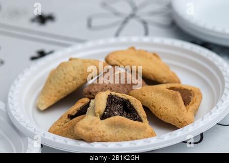 Hamantaschen. (ozen haman). La nourriture juive pour Purim. Pâte croustillante triangulaire, farcie de dattes, halva et chocolat, sur une plaque blanche. Banque D'Images