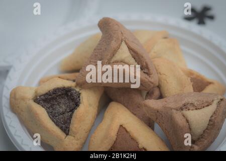 Hamantaschen. (ozen haman). La nourriture juive pour Purim. Pâte croustillante triangulaire, farcie de dattes, halva et chocolat, sur une plaque blanche. Banque D'Images