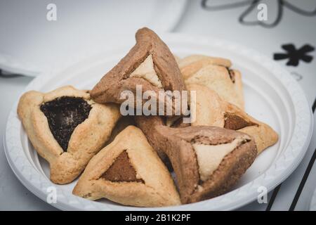 Hamantaschen. (ozen haman). La nourriture juive pour Purim. Pâte croustillante triangulaire, farcie de dattes, halva et chocolat, sur une plaque blanche. Banque D'Images