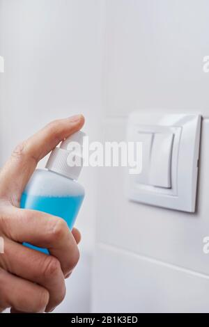 gros plan d'un homme caucasien qui désinfecta le commutateur d'éclairage en vaporisant un désinfectant bleu à partir d'une bouteille Banque D'Images