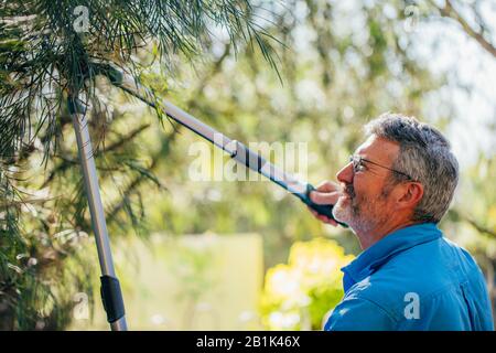 Homme senior coupe des branches d'arbres de tonte à l'extérieur dans le jardin. Banque D'Images