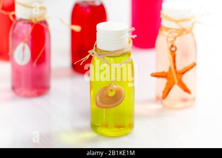 Collection de petites bouteilles transparentes avec des liquides aromatiques jaunes et roses vibrants décorés de coquillages et de étoiles de mer sur une table blanche Banque D'Images