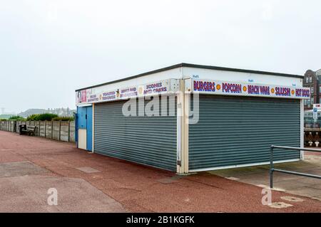 Un grand kiosque à toit plat solidement fixé avec des écrans à volets roulants se tient sur la surface rougeâtre de l'esplanade à côté d'un mur en béton Banque D'Images