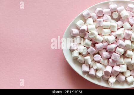 Mini guimauves roses et blanches en plaque blanche sur fond rose avec espace libre pour le texte Banque D'Images