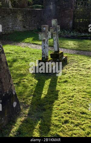 Deux croix en pierre rétroéclairées, jetant de longues ombres, dans la cour de St Mary Magdalene, Castle Ashby, Northamptonshire, Royaume-Uni Banque D'Images