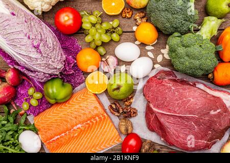 Tendance paleo/pegan régime. Concept de nourriture saine et équilibrée. Ensemble de produits frais, viande crue, saumon, légumes et fruits. Vieux fond de planches en bois Banque D'Images