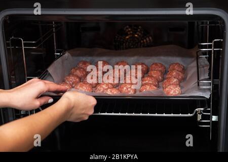 Les mains féminines font des boulettes de viande dans le four. Boulettes de viande brutes suédoises. Viandes de bœuf frites maison. Cuit sur parchemin Banque D'Images