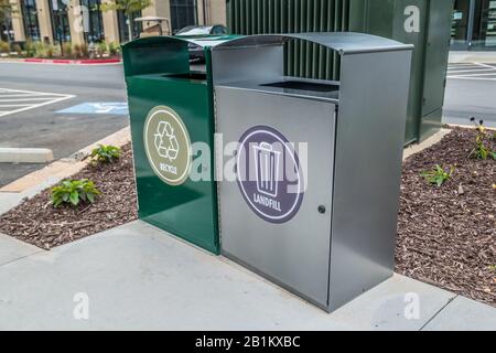 Deux poubelles en métal côte à côte, l'une pour les matières recyclables et l'autre pour la mise en décharge sur un patin en ciment dans un parking devant la vue d'angle des bâtiments Banque D'Images