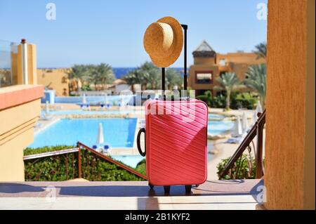 Voyage, vacances d'été et concept de vacances. Valise rose avec chapeau sur l'arrière-plan de la piscine de l'hôtel en Egypte Banque D'Images