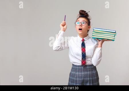 Une jolie adolescente aime étudier. La écolière possède une pile de livres et élève exclaimely le stylo vers le haut. La littérature d'étude. Une éducation appropriée. École club après la classe. Apprendre une langue étrangère. Banque D'Images