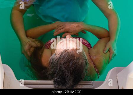 Vue rapprochée de la femme âgée penchée sur l'échelle de la piscine. Détente alors que la jeune femme donne un massage à la main pour la relaxation des muscles Banque D'Images