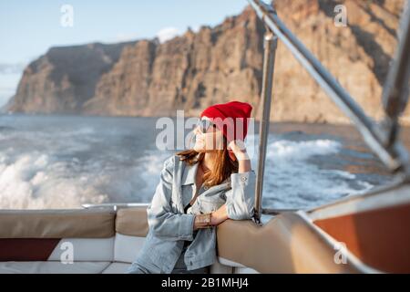 Portrait d'une jeune femme voyageur vêtue de façon décontractée avec un chapeau rouge et un Jean naviguant sur un yacht près de la côte rocheuse. Concept d'un style de vie et d'un voyage sans souci Banque D'Images