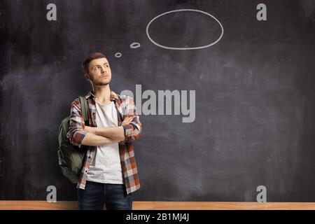 Étudiant masculin pensif devant un tableau noir avec une bulle de pensée Banque D'Images