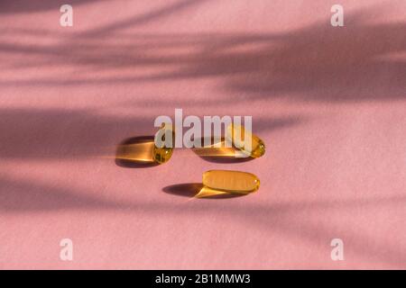 Capsules de gélatine jaune d'huile sur fond rose avec ombre de fleur, vitamines et concept antioxydant Omega 3, morue de foie ou huile d'onagre de soirée pour les soins de santé. Le Minimalisme. Espace de copie. Banque D'Images