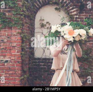 Femme de culture portant une robe longue rose chic boho et tenant un magnifique bouquet avec des rubans sur la jetée dans le parc Banque D'Images