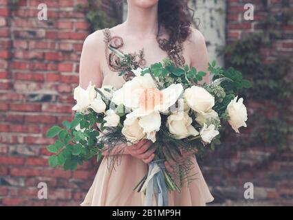 Femme de culture portant une robe longue rose chic boho et tenant un magnifique bouquet avec des rubans sur la jetée dans le parc Banque D'Images