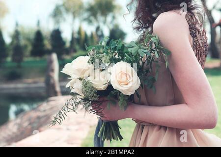 Femme de culture portant une robe longue rose chic boho et tenant un magnifique bouquet avec des rubans sur la jetée dans le parc Banque D'Images