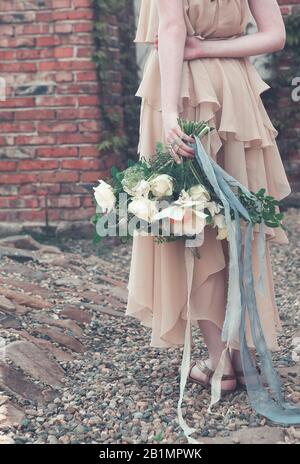 Femme de culture portant une robe longue rose chic boho et tenant un magnifique bouquet avec des rubans sur la jetée dans le parc Banque D'Images