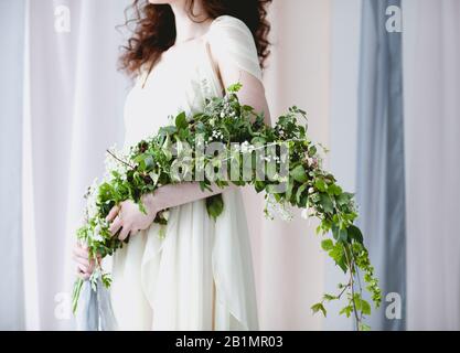 Chabillez une femme pieds nus dans une élégante robe de mariage blanche avec un grand bouquet de petites fleurs blanches et un feuillage vert se tenant dans une couleur pastel transparente c Banque D'Images