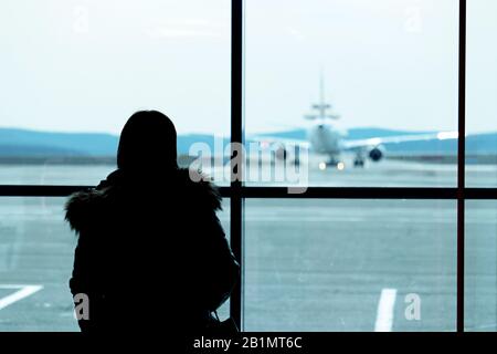 Silhouette d'une femme dans le bâtiment de l'aéroport en regardant l'avion sur le tarmac à travers le verre. Concept de vol en attente, passager en retard Banque D'Images