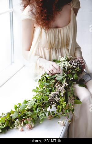 Femme de culture dans une élégante robe de mariage blanche avec grand bouquet de petites fleurs blanches et de feuillage vert debout parmi des rideaux de couleur pastel transparents Banque D'Images