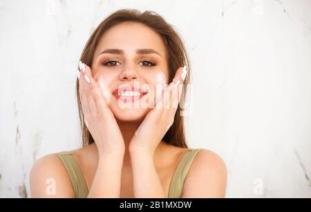 Belle jeune femme brune caucasienne se lavant le visage avec de la mousse. Concept cosmétique Banque D'Images