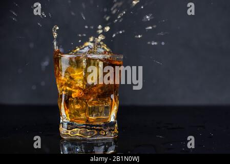 buvez de l'alcool et de la glace avec des gouttes dans un verre sur fond noir Banque D'Images