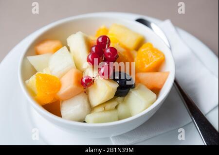 Bol de salade de fruits frais comprenant le melon de cantaloup, l'orange, l'ananas, recouvert d'une branche décorative de lingonberry Banque D'Images