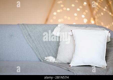 Canapé gris doux avec oreillers blancs contre un mur brun flou avec des lumières comme symbole de chaleur et de confort à la maison Banque D'Images